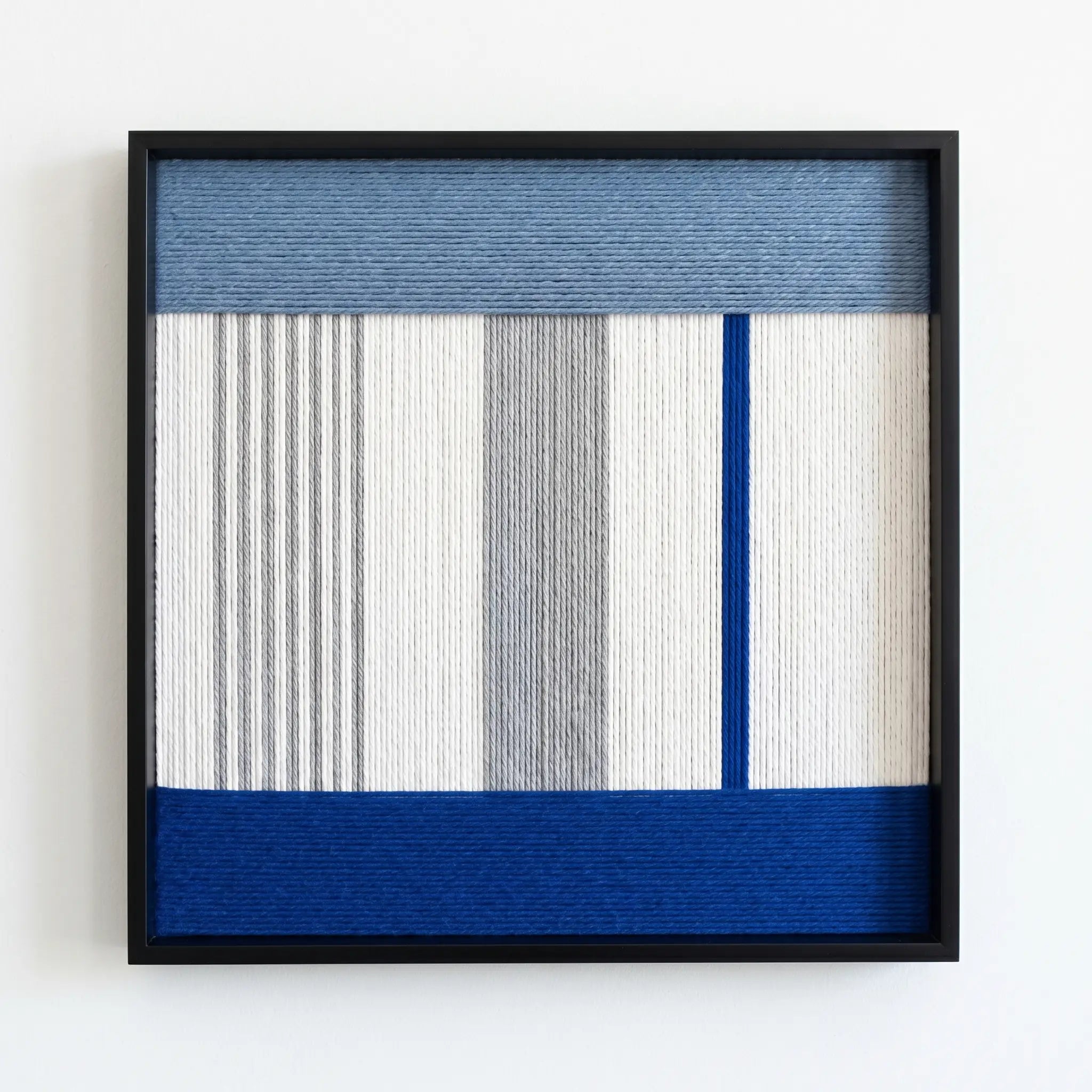 Professional studio shot of the Absolute Zero hand-woven wool wall art featuring blue and grey geometric patterns in a black frame.