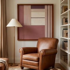 Framed Ballet Whispers textile wall art displayed in a cozy reading nook, hanging above a classic brown leather armchair next to a floor lamp and bookshelf.