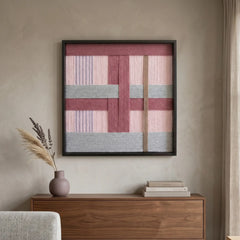 Square pink and grey wool wall art hanging above a dark wood sideboard with minimalist vases and natural lighting.