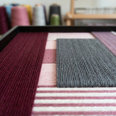 An angled close-up of the fiber wall art in a studio, highlighting the multi-directional structural layering of the hand-wrapped yarn.