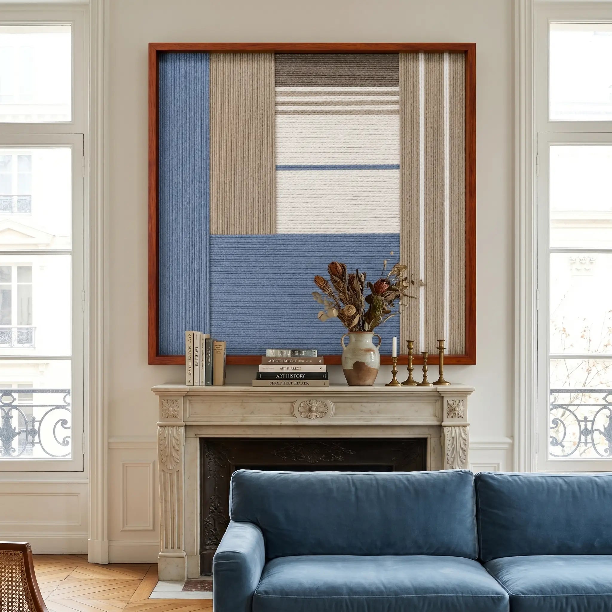 Striking square hand-woven wool tapestry positioned perfectly above a classic fireplace mantel in a well-lit living room with a matching blue velvet sofa.