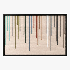 Frontal studio shot of the Chromatic Rain hand-woven wool wall art featuring colorful vertical dripping yarn stripes on a beige background in a black frame.