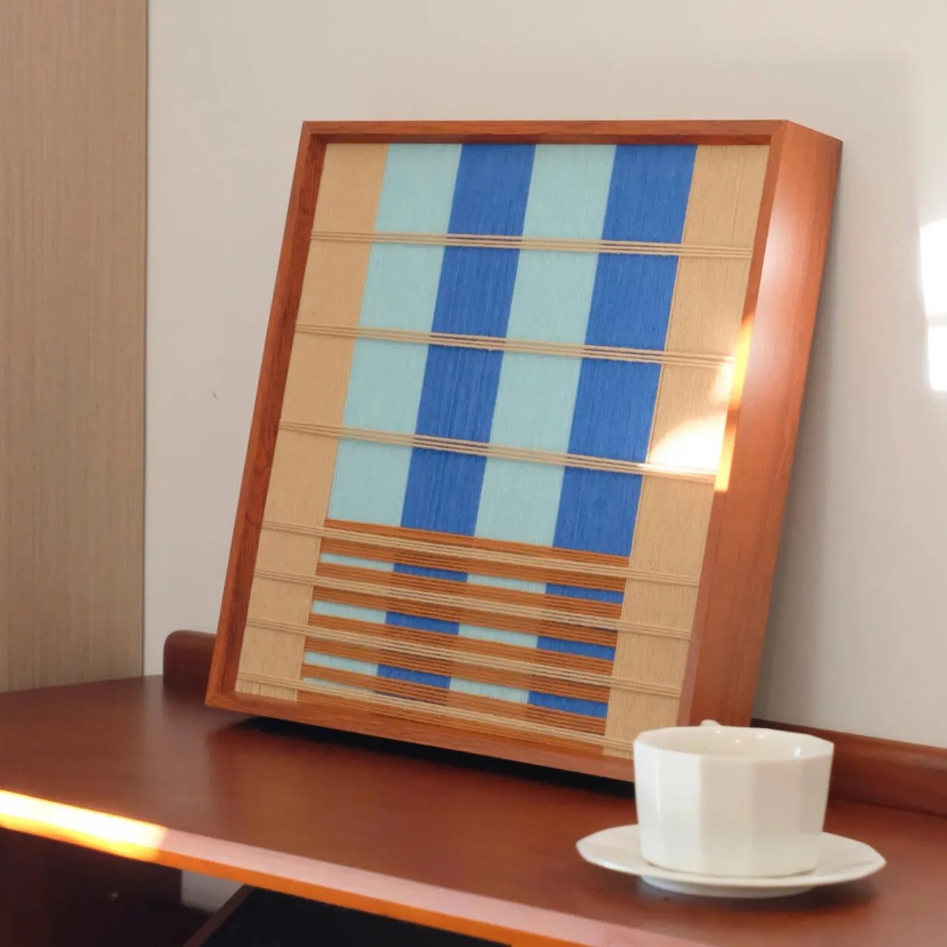 Chuan yarn wall art displayed on a table next to a cup, showcasing precise stripe alignment and smooth wool texture