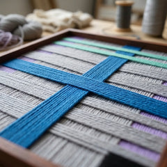 Angled macro shot of the Cobalt Window fiber art highlighting the raised blue intersecting yarn over horizontal grey and purple background layers.