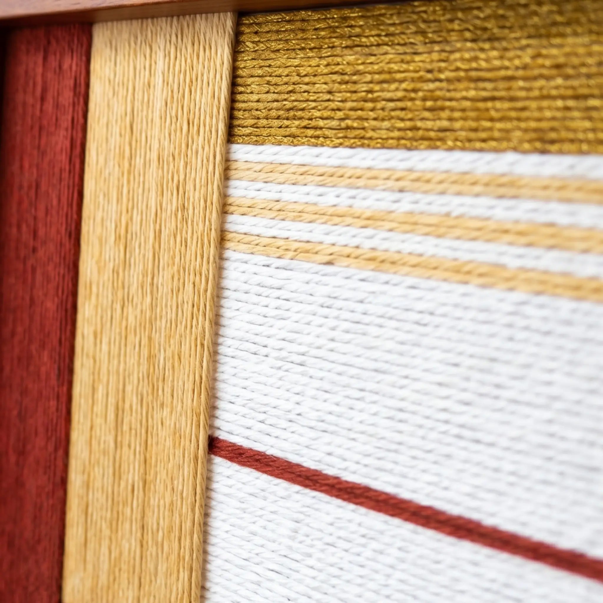 Extreme macro close-up of the Crimson Daybreak hand-woven textile art highlighting the textured crimson red, mustard yellow, and white yarn details.