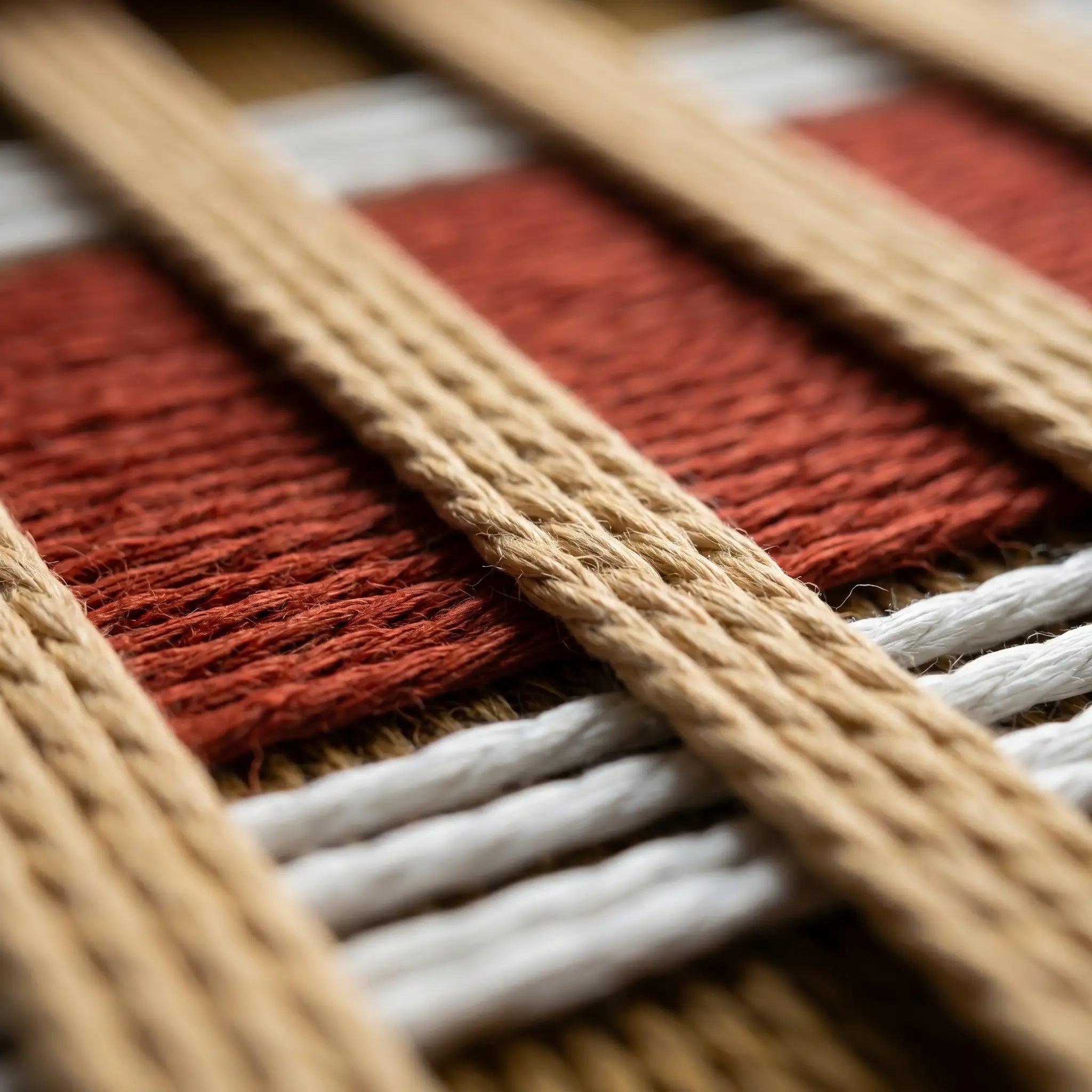 Extreme low-angle macro shot of the Gilded Coronation hand-woven textile art lying flat, highlighting the textured rust-red and mustard-gold vertical yarn stripes.