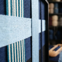 An angled close-up view of the textured fiber wall art in a studio, highlighting the structural multi-directional layering of the wool yarn.