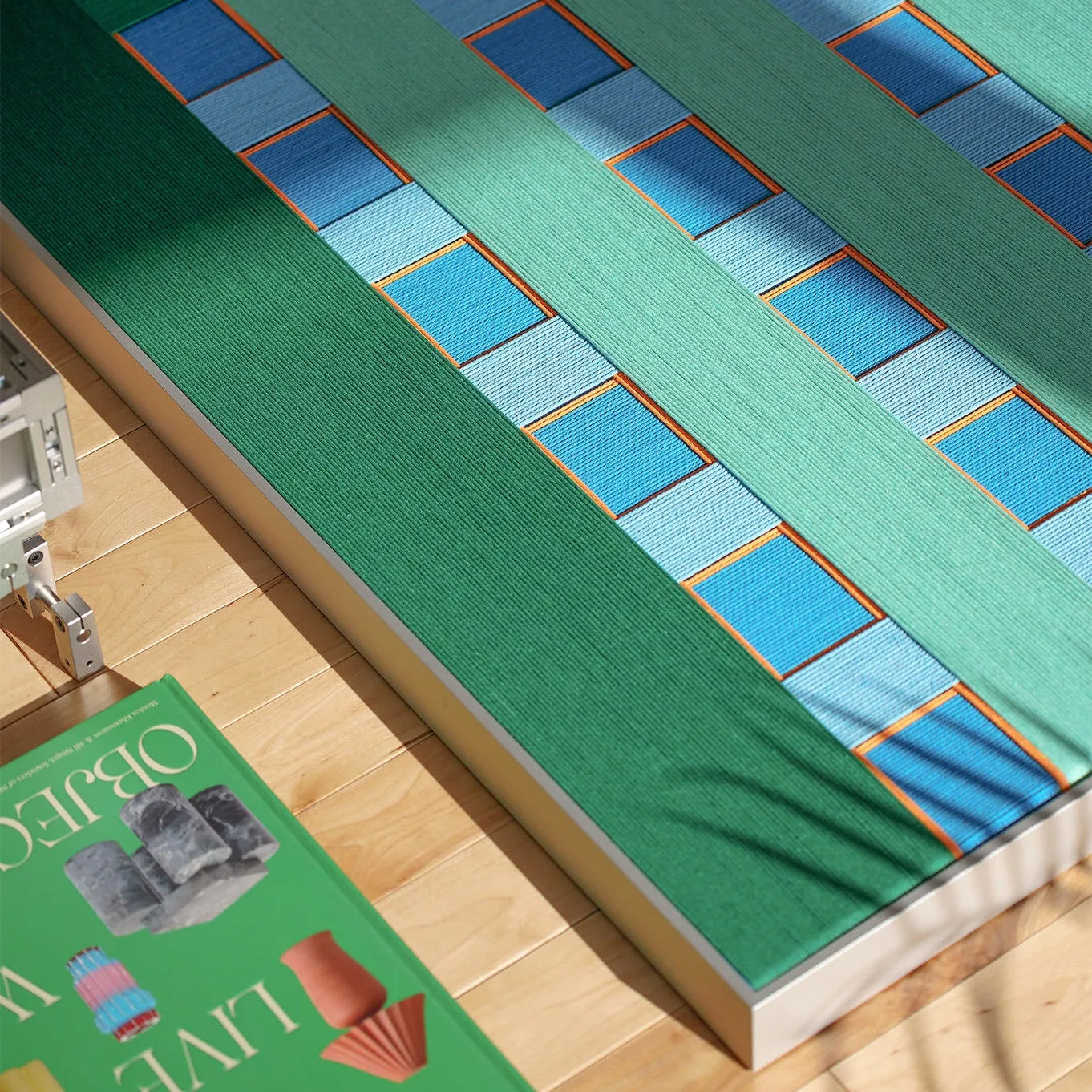 Angled close-up view highlighting the soft wool texture and intricate hand-woven geometric pattern in fresh green, ocean blue, and sunny yellow tones.