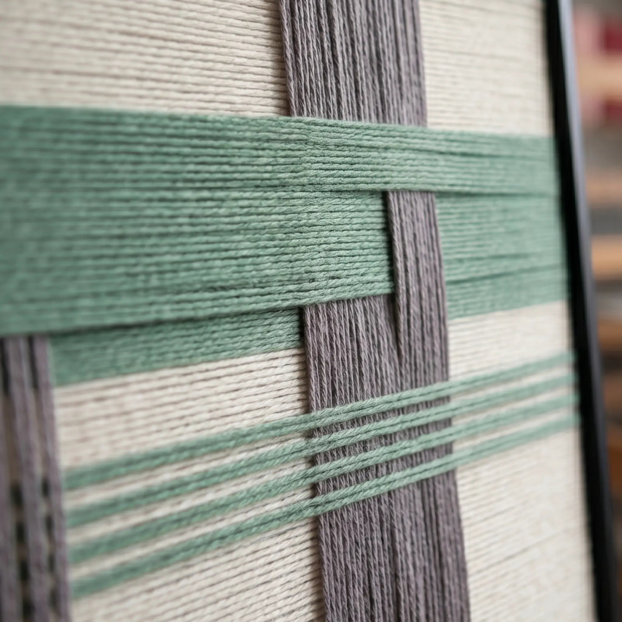 Macro close-up of the Muted Spring fiber art highlighting the structural layering of raised sage green yarn over vertical grey and cream background bands.