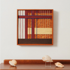 A single framed woven wall hanging featuring a central orange textured square surrounded by blue and white vertical lines on a dark background.