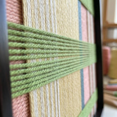 Macro close-up of the Pastoral Lullaby fiber art highlighting the raised spring green yarn woven over pastel pink and yellow background layers.