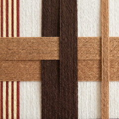 Macro shot of the hand-woven wool texture showing the intricate interlocking brown and terracotta yarn patterns.