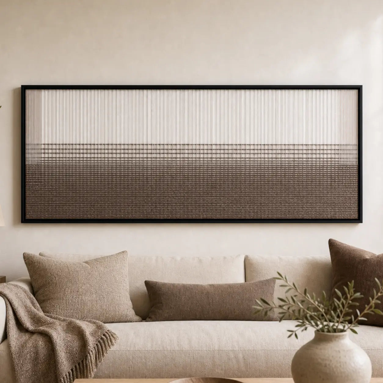 Large framed Quiet Thread hand-woven wall art hanging elegantly above a cozy cream sofa in a neutral living room.