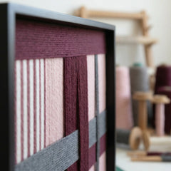 Close-up side view of Rose Coordinates hand-woven wool art showing the deep burgundy, dusty rose, and grey yarn textures in a sleek black frame.