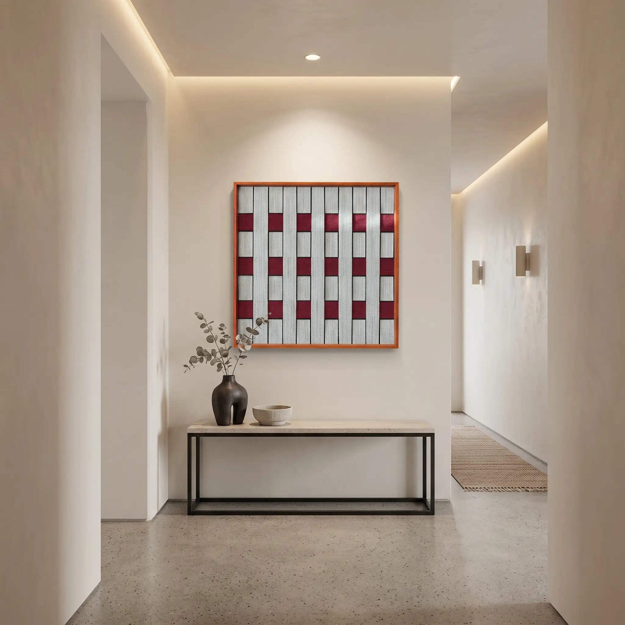 Framed textured fiber wall art hanging above a minimalist black console table in a modern, well-lit hallway corridor.