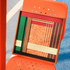 Saint Christmas yarn wall art leaning on a wooden chair, illustrating its square format, sturdy frame, and festive stripe design