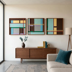 Framed geometric textile wall art triptych displayed above a wooden cabinet next to a white sofa with a blue accent pillow in a sunlit room.