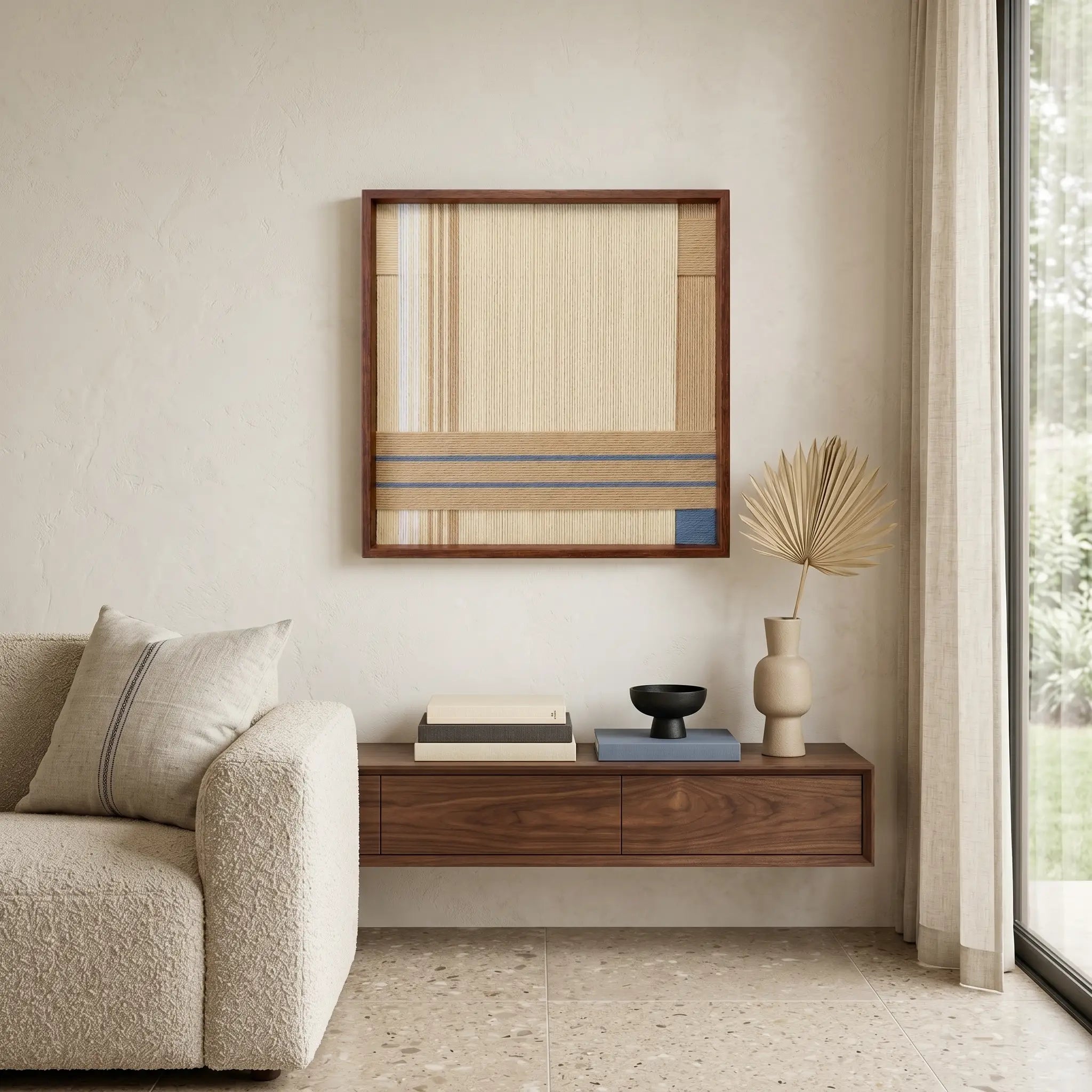 Large hand-woven wool wall art in beige and blue tones displayed above a floating walnut shelf in a minimalist living room.
