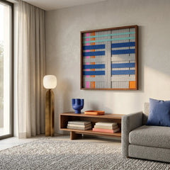 Large square Silent Dopamine fiber wall art featuring blue, grey, and orange geometric hand-woven patterns hanging above a low wooden console in a modern living room.