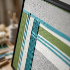 Detailed side view of the framed fiber art in a workshop setting, showcasing the depth and three-dimensional wool winding.