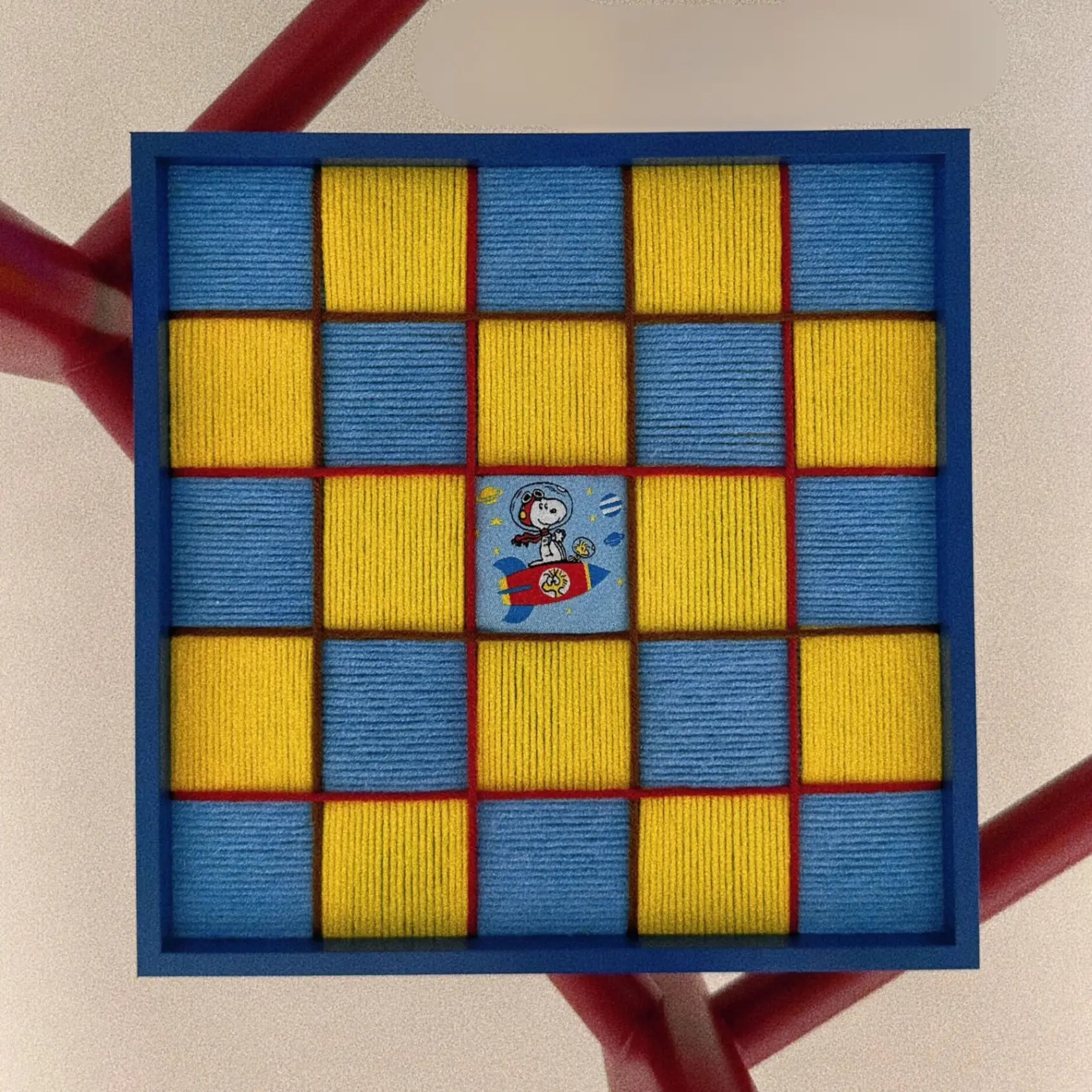 Close-up front view of the textured fiber wall art showing the yellow and blue hand-woven checkerboard pattern and a central Snoopy space patch.