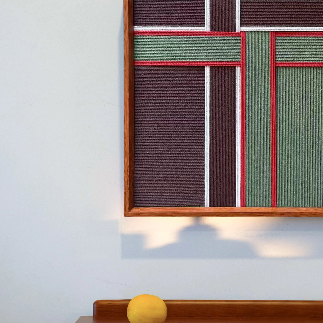 Angled shot capturing the depth of the wooden frame and the tactile surface of the hand-woven red and green wool fibers.