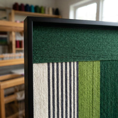 Side profile of the green and neutral wool wall art in a workshop setting, showcasing the depth of the woven threads.
