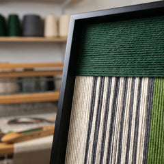 Close-up shot of the top corner of the framed fiber art showing the horizontal and vertical hand-woven wool textile patterns.