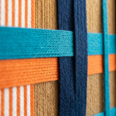 Macro shot of the vibrant hand-wrapped wool yarn showing the interlocking navy and orange patterns and high-quality textile detail.