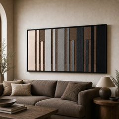 Large framed Umber Columns hand-woven wall art hanging elegantly above a cozy brown sofa in a warm, neutral living room setting.