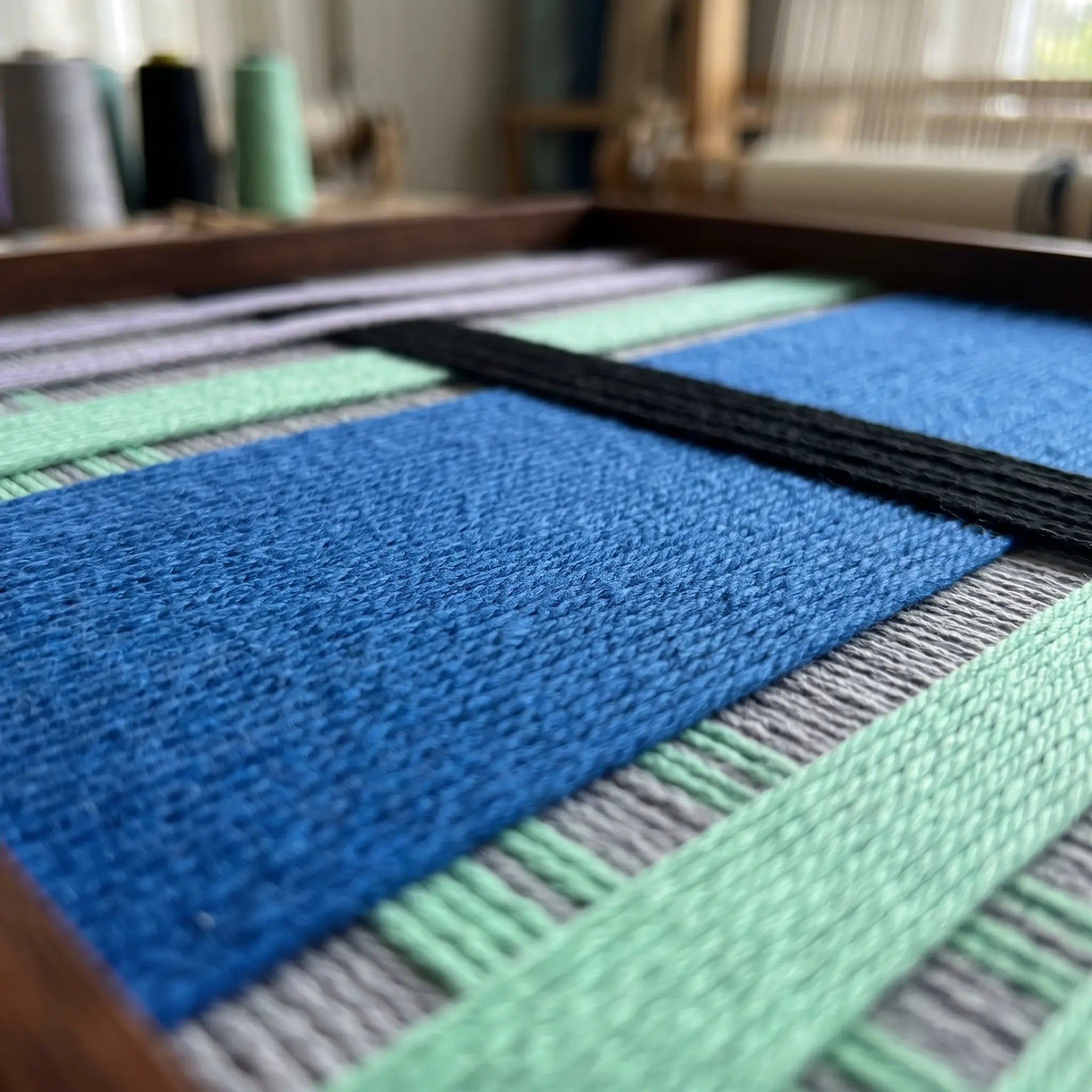 Extreme close-up of the Winter Aurora tapestry showcasing the dense, high-texture cobalt blue and black hand-wrapped wool yarn within a wooden frame.
