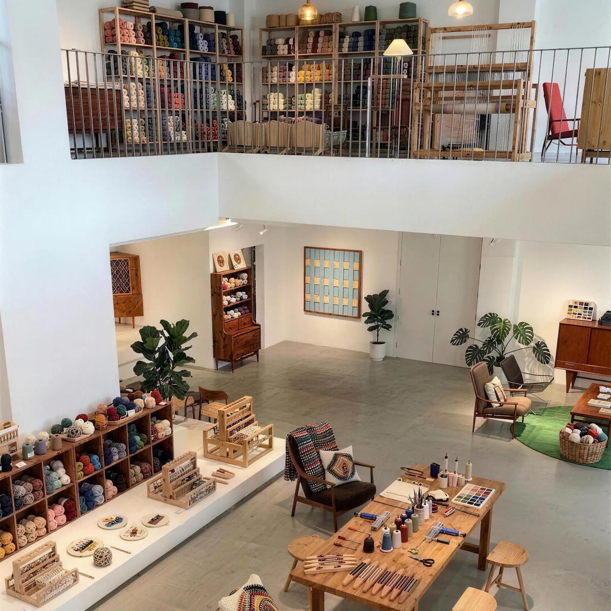 Inside the modern two-story Aassort Textile Art studio and showroom. The bright, minimalist space features beautifully organized colorful yarn supplies, professional weaving tools, and a large loom, reflecting a warm and high-end contemporary textile art creation environment.