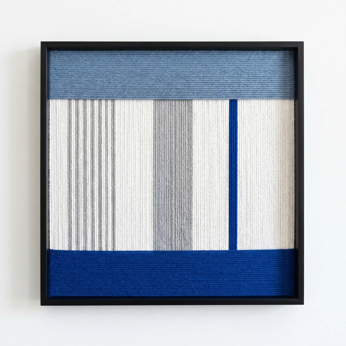 Professional studio shot of the Absolute Zero hand-woven wool wall art featuring blue and grey geometric patterns in a black frame.