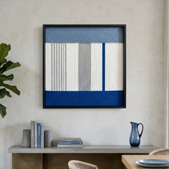 Modern hand-woven wool tapestry displayed above a minimalist grey console table with blue decorative accents in a sunlit room.