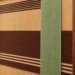 Macro close-up of the Amber Pine textile art highlighting the structural layering of the raised green vertical yarn intersecting over dark brown and tan horizontal bands.