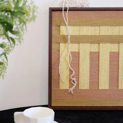 Hand-held view of Autumn Mountain yarn wall art showing its square proportions, precise stripe alignment, and robust wood frame.
