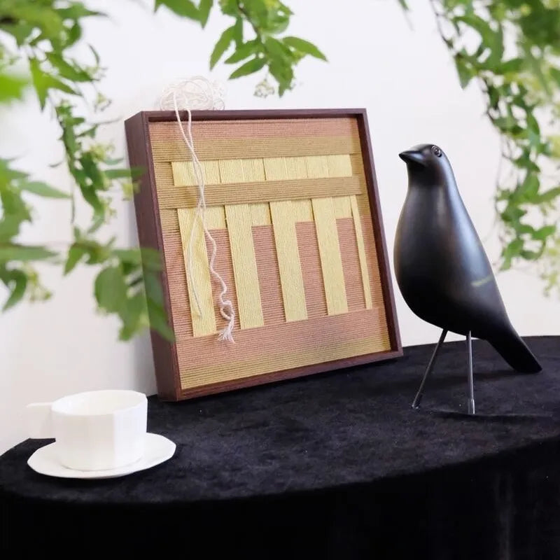 Autumn Mountain yarn wall art leaning against a tabletop plant vase, showcasing its tactile looped wool texture and warm earth-tone stripes.
