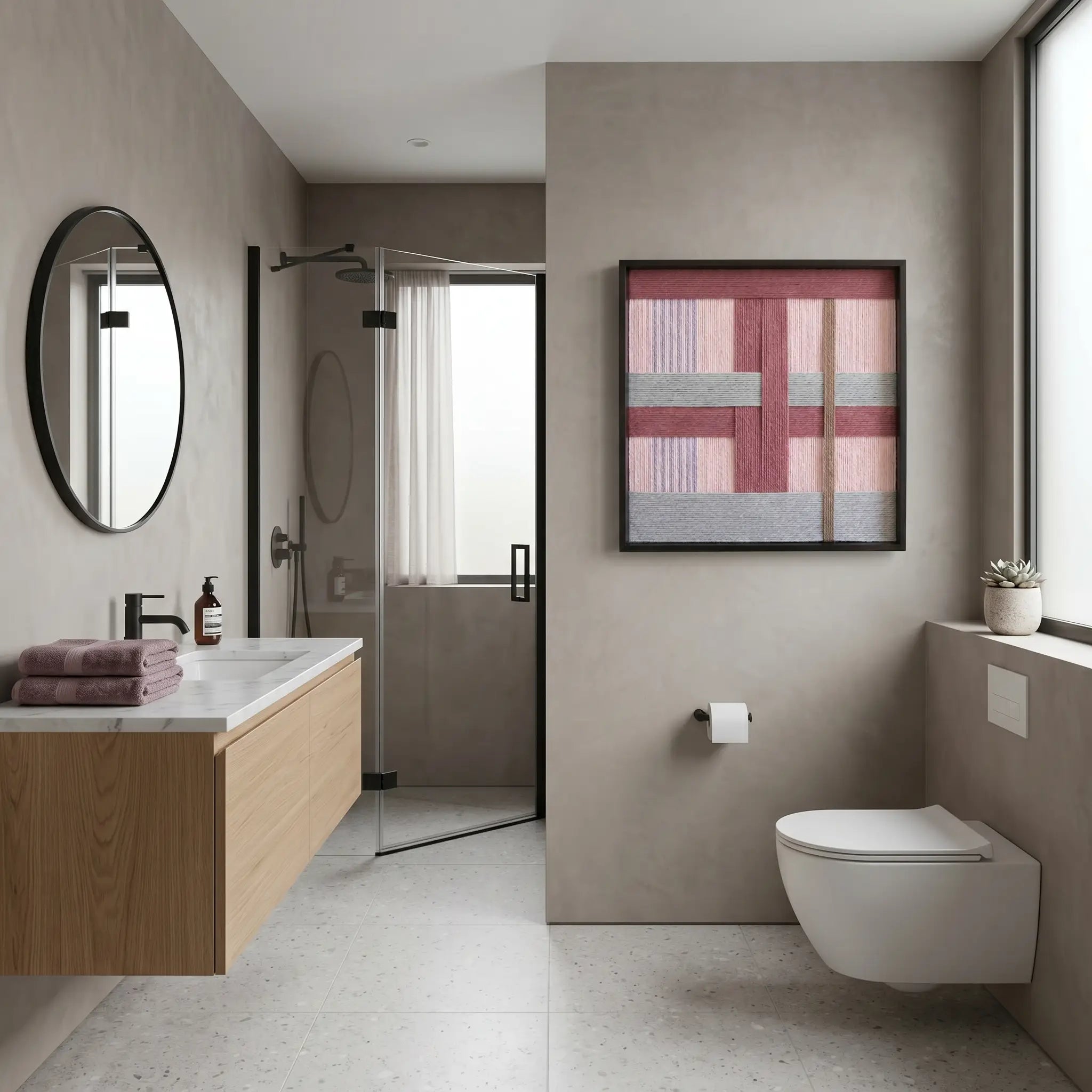Framed textured fiber wall art styled in a contemporary luxury bathroom with a light wood floating vanity and neutral stone tiling.