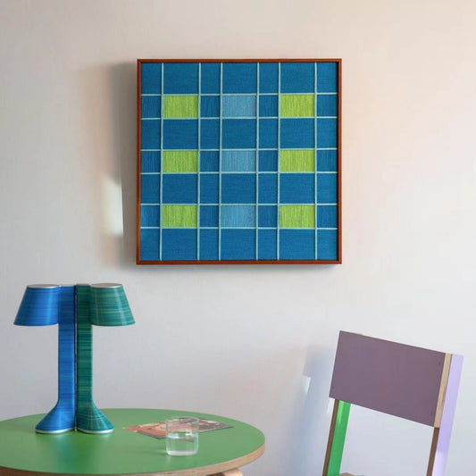 The dark blue variation of the North Sea Poem fiber art displayed above a green table with a modern blue lamp, creating a cohesive color palette.