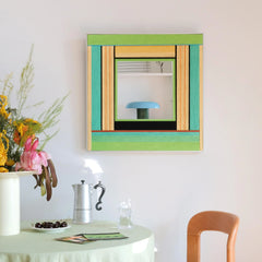 Breathing Like Fresh Grass hand‑woven yarn mirror wall art featuring alternating mint green, grass green, and natural wood stripe borders framing a central mirror panel, displayed above a small table with vase.
