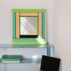 Breathing Like Fresh Grass mirror art styled on a white shelf with a potted plant and books, showcasing its crisp green stripe design and reflective center.
