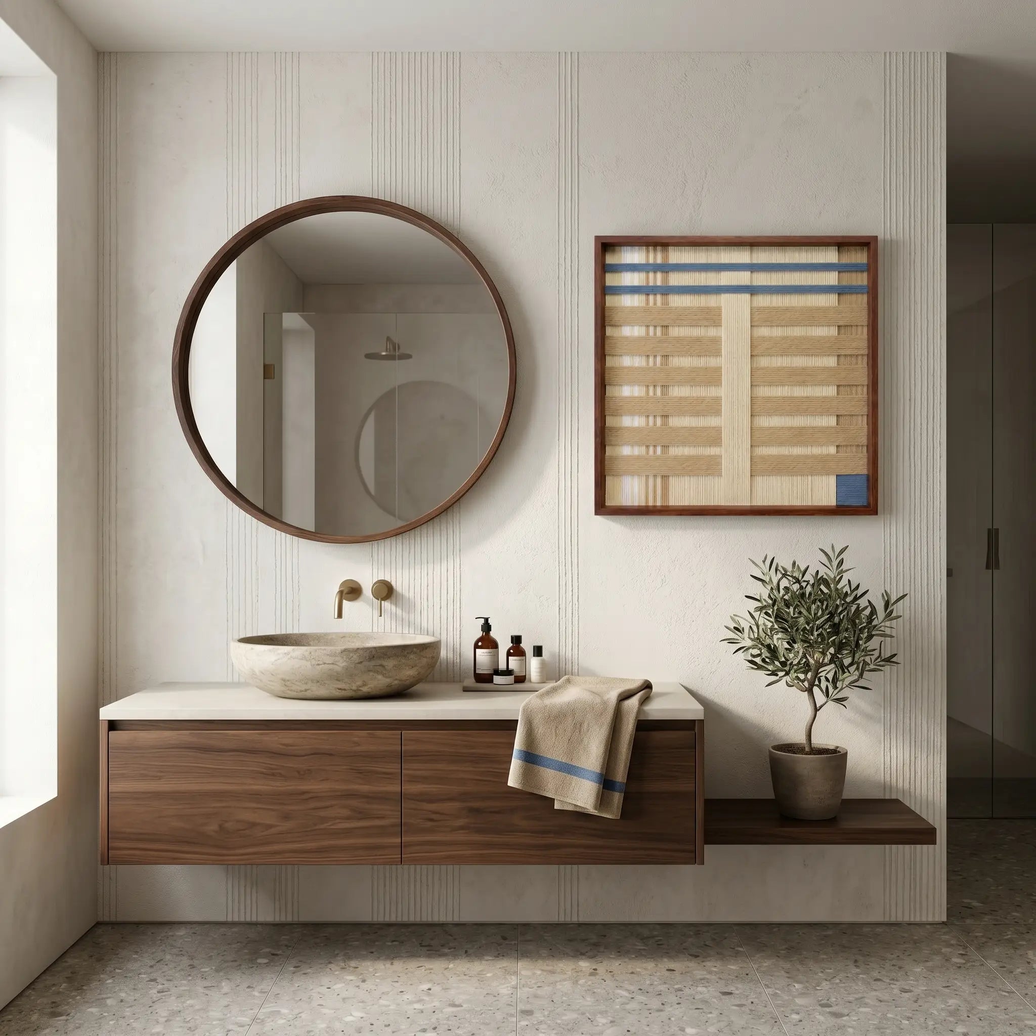 Framed hand-woven wool tapestry displayed in a luxury bathroom above a floating wooden vanity next to a large circular mirror.