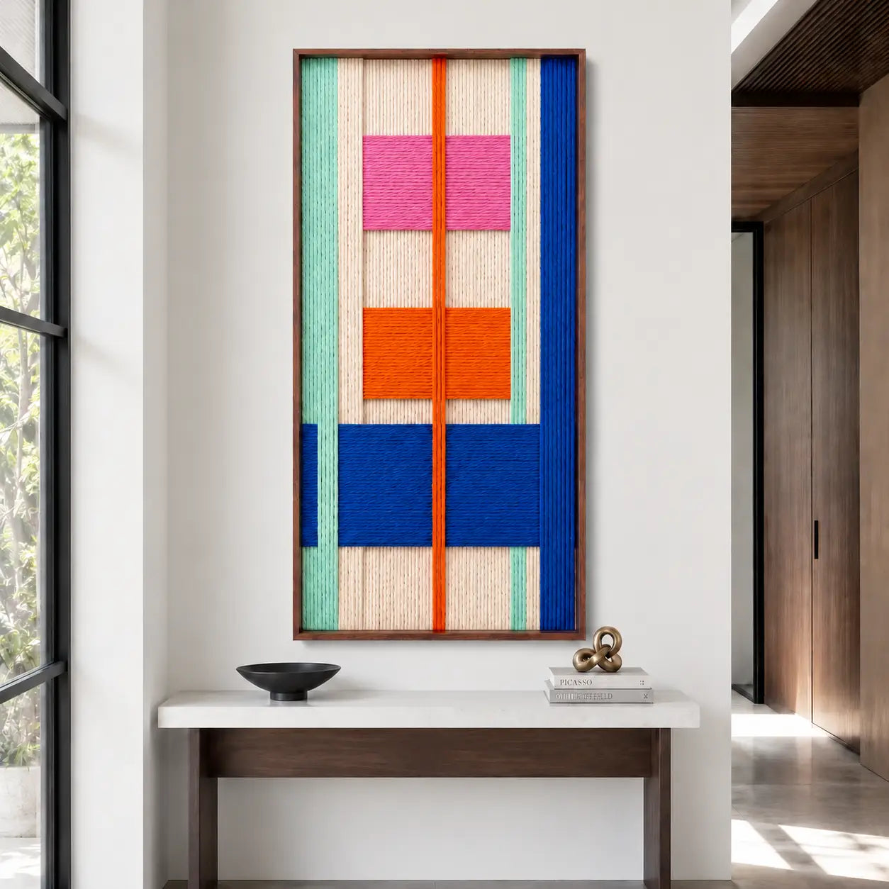 Clean entryway setting highlighting the hand-woven wool tapestry hanging above a sleek white console table with minimalist decor objects.