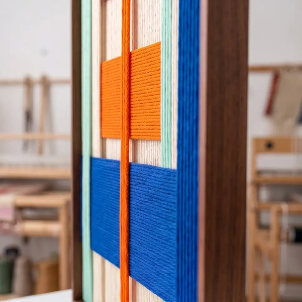Side profile view of the framed hand-woven wool tapestry emphasizing the textured multi-layered yarn structure and high-quality metal framing.