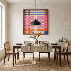 Large square California Afterglow fiber wall art featuring vibrant pink, orange, and blue hand-woven wool patterns hanging in a modern dining room with cane chairs and a wood table.
