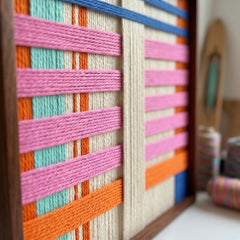 Close-up macro shot of the California Afterglow fiber art highlighting the bright pink, orange, and blue hand-wrapped wool yarn and structural layering within a wooden frame.
