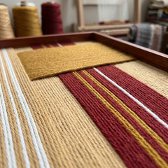 Angled close-up shot of the Carmine Pulse textile art showcasing the raised dimensional mustard yellow patch over textured red and beige hand-woven wool stripes.