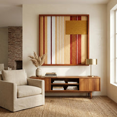 Large square Carmine Pulse hand-woven wall art hanging elegantly above a wooden media console next to a light beige armchair in a sunlit living room.