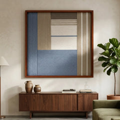 Framed Cerulean Mist textile wall art displayed in a bright living room, hanging above a dark wooden sideboard adorned with ceramic vases.