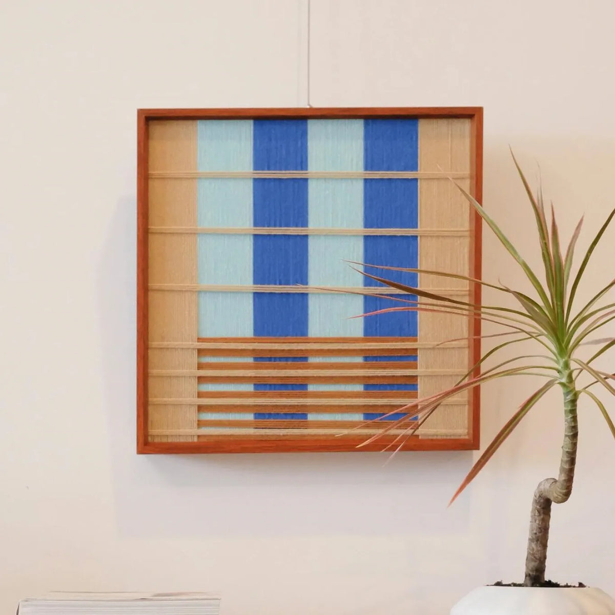 Chuan hand-woven yarn wall art featuring alternating sky-blue and natural beige vertical stripes in a natural wood frame, displayed on a console table
